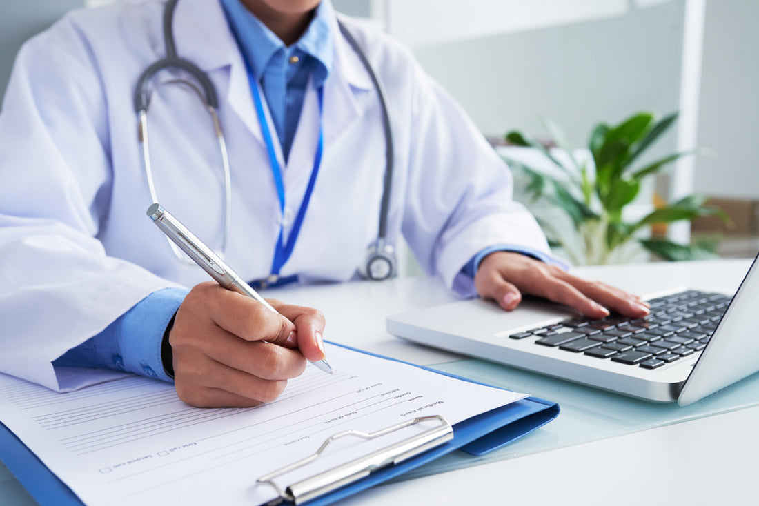 Medico prende appunti su una scheda paziente. Con PC. ambulatorio. Dottore
